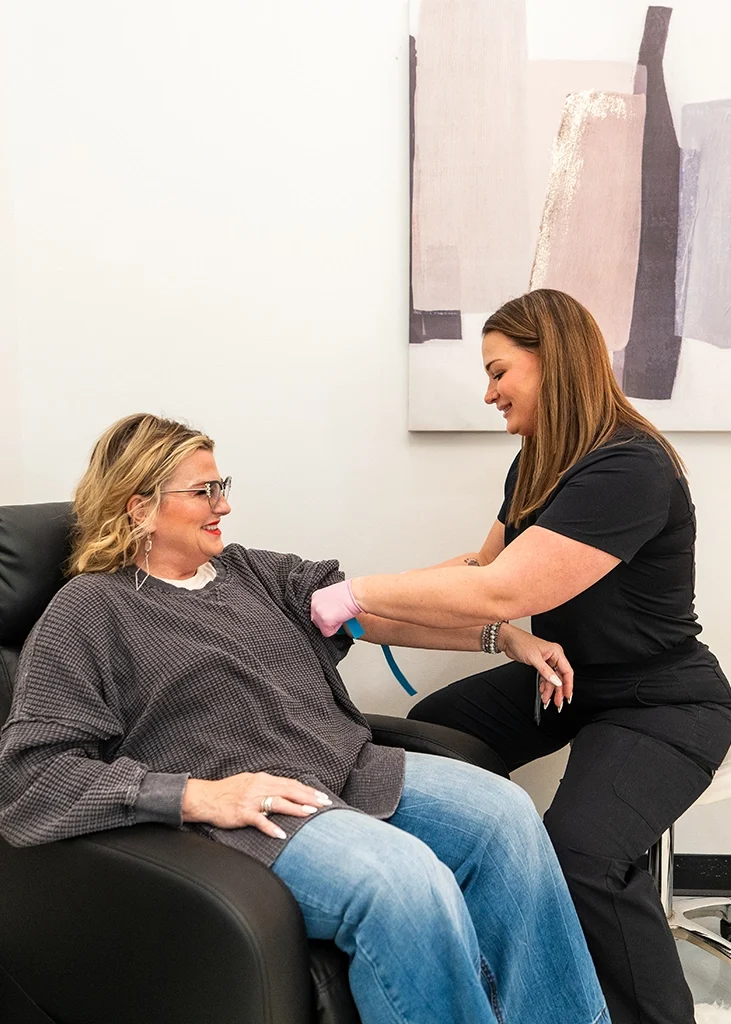 Med spa provider preparing a client’s arm for IV therapy while the client sits comfortably in a treatment chair.